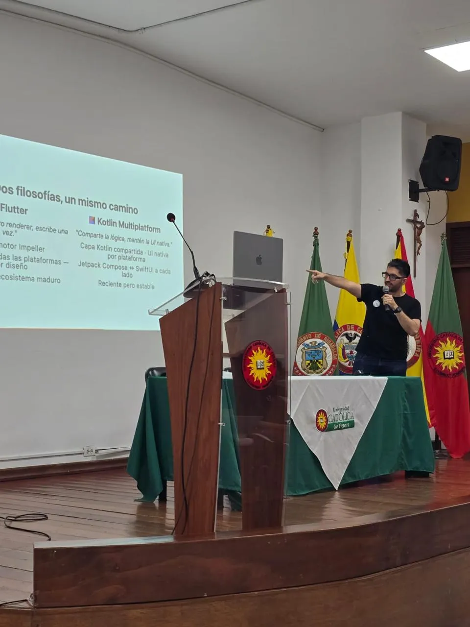 Sergio on stage pointing at a slide titled 'Dos filosofías, un mismo camino' comparing Flutter and Kotlin Multiplatform