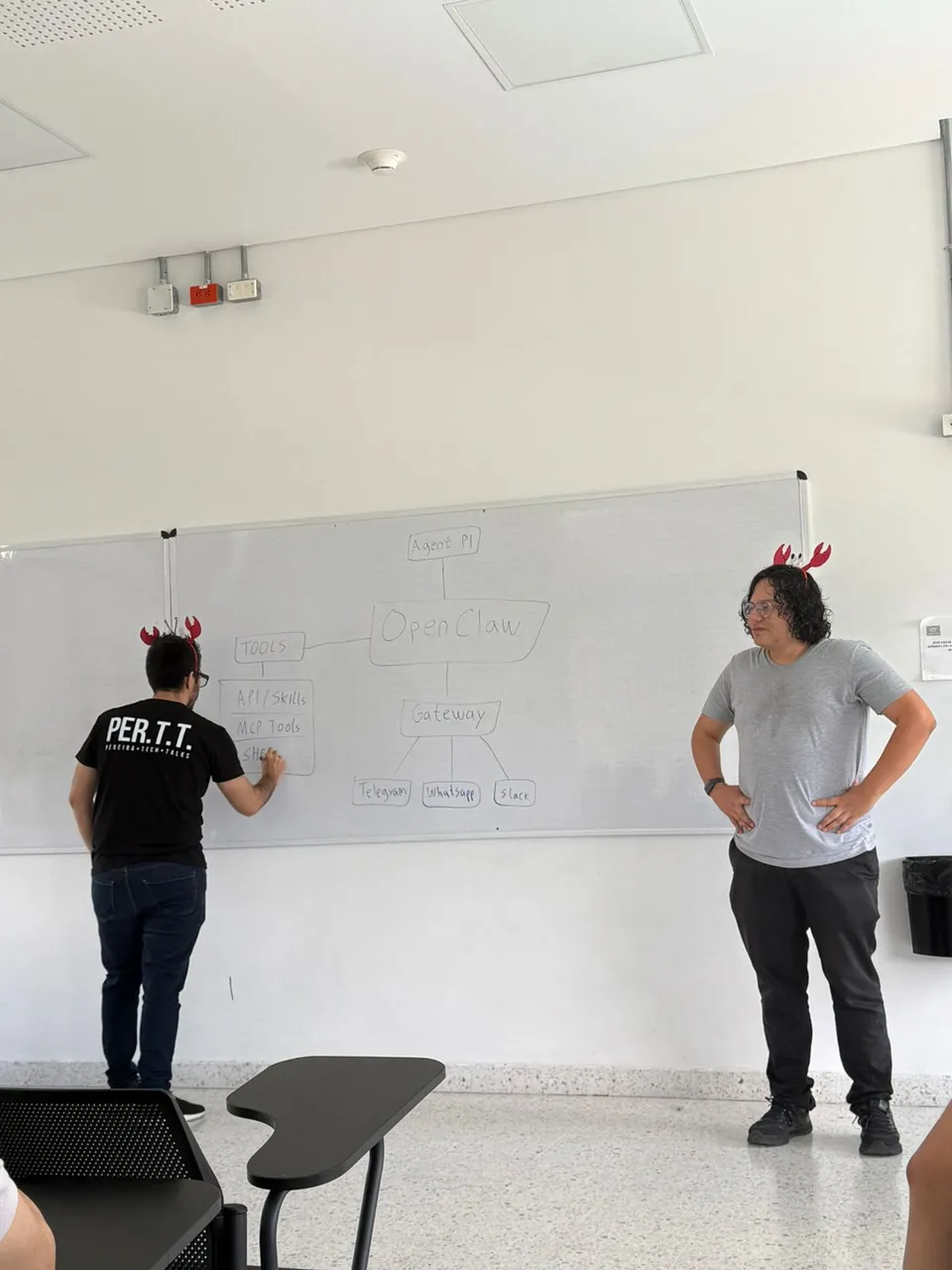 Two presenters at a whiteboard with a hand-drawn OpenClaw architecture diagram: an agent connected to OpenClaw, a gateway fanning out to Telegram, WhatsApp and Slack, and a tools box listing APIs, skills, MCP tools and shells